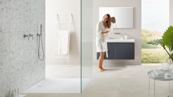 Woman drying her hair with a towel in a bathroom with open shower and large tiles in terrazzo style