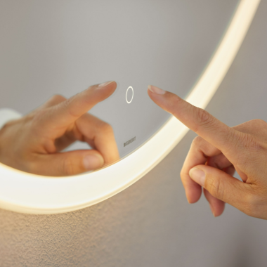 Hand operating touch sensor switch on Geberit Option Round mirror (© Geberit)