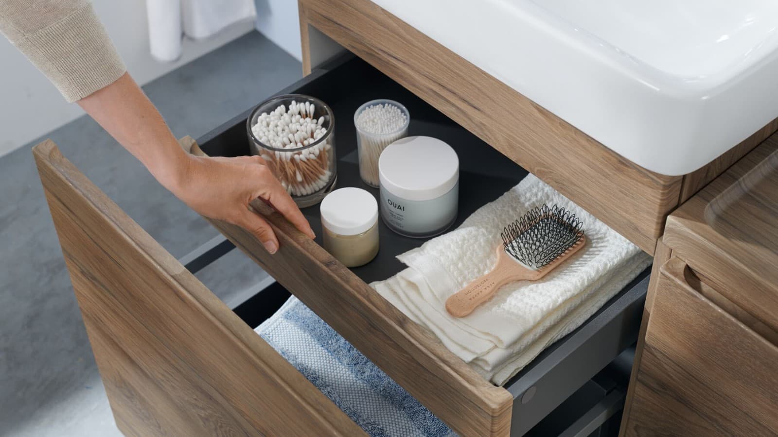 A hand opens one of the drawers of the Geberit Renova Plan washbasin cabinet in a natural wood design A hand opens one of the drawers of the Geberit Renova Plan washbasin cabinet in a natural wood design